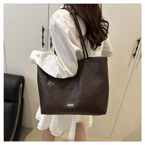 Detailed view of dark brown woven texture tote bag with fashion label on white dress