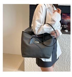 Detail shot of a dark grey woven tote bag on shoulder, showing texture and metal logo