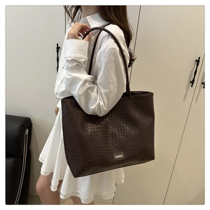 Detail of dark brown woven tote bag showing fashion label and texture on model shoulder