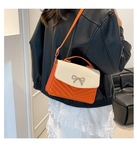 Detail of orange handbag with woven flap and silver bow worn by a model in leather jacket
