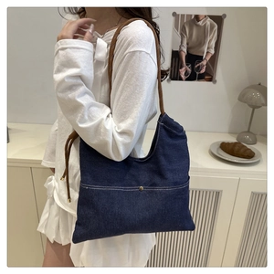Detail of blue denim shoulder bag featuring unique brown woven rope strap and metal snap button