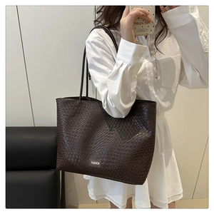 Detailed view of dark brown woven tote bag with Fashion tag worn by model in office