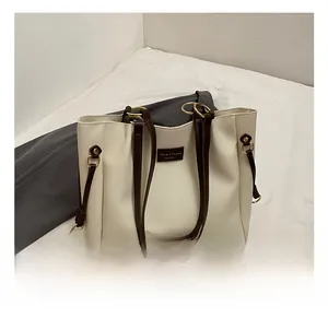 Close-up of beige tote bag with brown straps, drawstring detail and golden hardware