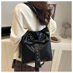 Detail of black leather tote bag with crystal-encrusted bow on a model shoulder