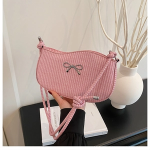 Detail of pink woven shoulder bag featuring silver bow ornament and cord strap