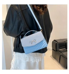 Detail of light blue crossbody bag featuring a metal bow and quilted stripe design