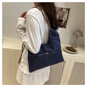 Minimalist navy denim tote bag with brown rope straps worn by a model in a cozy room
