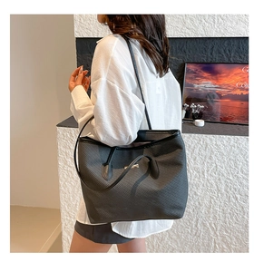 Detail of grey woven tote bag with silver logo on a shoulder-carry model view