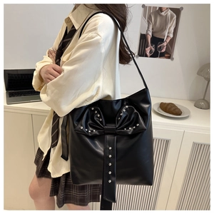 Detail of black PU leather shoulder bag with large bow and silver rivet studs on model