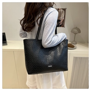 Detailed view of black woven tote bag with Fashion label worn over a model's shoulder