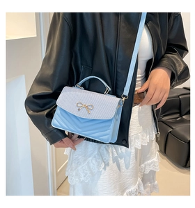 Detail of light blue shoulder bag with woven flap and gold bow accessory on a model