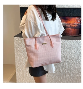 Detail view of pink woven tote bag with leather straps and metal plate accent