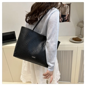 Detail of a large black woven tote bag with shoulder straps and Fashion label