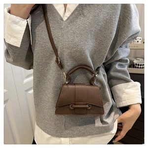 Detailed view of brown lychee leather mini crossbody bag with trapezoid design on model