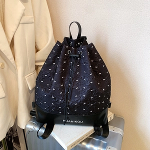 Black drawstring backpack with white bow embroidery on a silver metal suitcase
