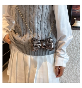Detail of a bow-shaped metallic mini bag with a sleek grey mirror finish and gold chain strap