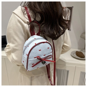 Close-up of a mini white backpack featuring red polka dots and a large bow with heart charm