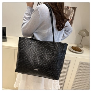 Detailed close-up of a large black woven tote bag with a minimalist fashion label tag