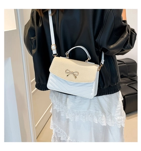 Detail of white and beige woven crossbody bag with gold bow and V-quilted pattern
