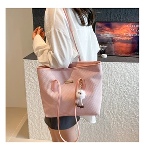 Detail of pink woven texture tote bag with gold metal plate and plush charm accessory