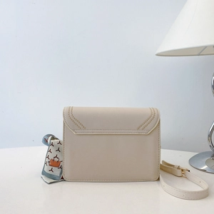Detail view of a beige crossbody bag with decorative golden stitching and silk scarf accessory