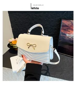Close-up of white crossbody bag with woven texture lid and golden bow hardware