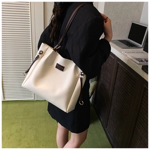 Minimalist beige tote bag shown from a side-rear angle on shoulder in workplace setting