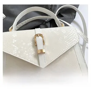 Detail of white embossed faux snake leather handbag with golden U-shaped metal buckle