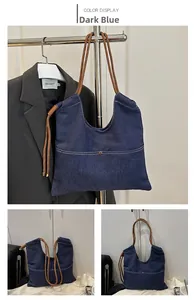 Detail view of large dark blue denim tote bag with brown woven rope shoulder strap and rivets