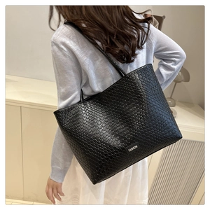Detail shot of a black woven leather tote bag featuring thin straps and fashion label