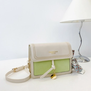 Close-up of contrast green shoulder bag with golden pendant and silk scarf detail