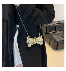 Dettaglio di una mini pochette dorata a forma di fiocco con una sottile tracolla a catena