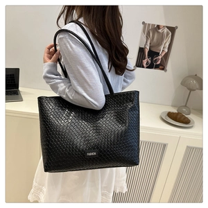 Detail of black woven texture tote bag with Fashion label and long shoulder straps