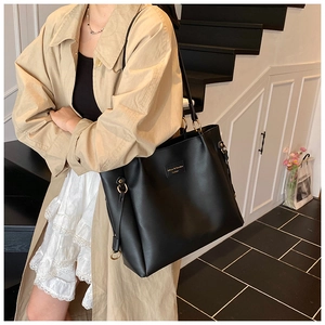 Detail of black matte leather tote bag with gold logo paired with a stylish trench coat