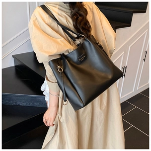 Detail of a large black matte leather tote bag with metallic ring and drawstring side