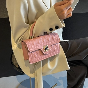 Elegant pink quilted handbag with gold clover lock held by woman in a beige suit
