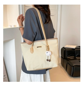 Detail of a large beige woven tote bag with brown straps and a cute plush charm