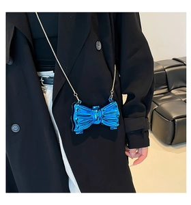 Dettaglio della mini borsa a fiocco blu metallizzato con catena dorata su modella