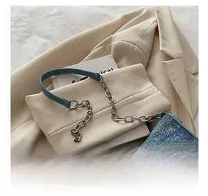 Detail of denim shoulder bag featuring silver chain strap on a beige blazer background