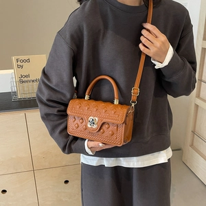 Brown quilted crossbody handbag with gold clover lock held by a model in casual wear