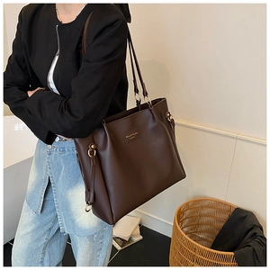 Detail of a large dark brown matte leather tote bag with a minimalist brand nameplate
