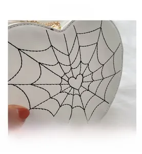 Macro detail of heart-shaped white handbag featuring black spiderweb stitching and gold chain