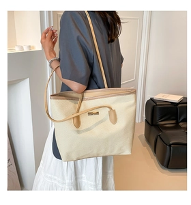Detail of beige woven texture tote bag with slim brown shoulder straps and metal plate