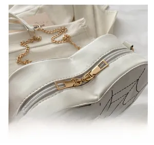Close-up of white heart bag showing smooth gold double zippers and spider web texture