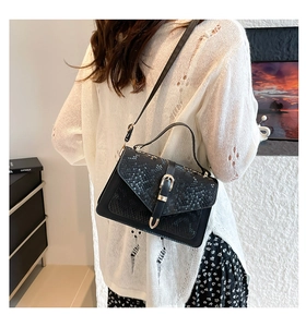 Fashionable black crossbody bag with snakeskin texture flap and gold buckle on female model