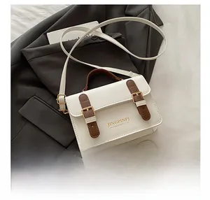 Detail of cream crossbody bag with brown handles and gold hardware on blazer background