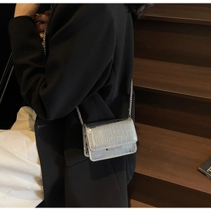 Detail of silver metallic mini bag with crocodile texture and metal chain strap