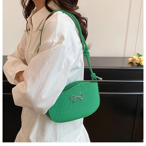Close-up of bright green woven shoulder bag with silver bow accent on female model