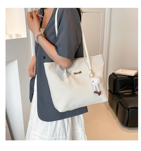 Detail of white woven tote bag featuring metal logo plate and plush toy charm