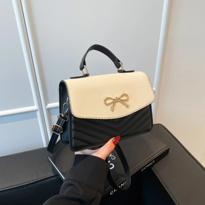 Minimalist beige straw and black leather crossbody bag with a gold bow buckle clasp